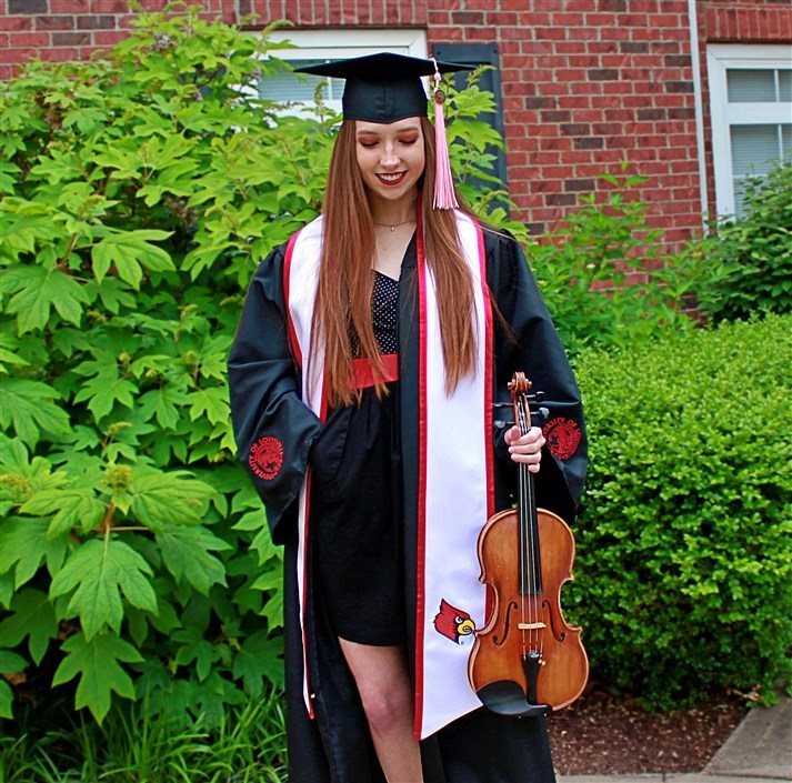 A person in a graduation gown holding a violin

Description automatically generated